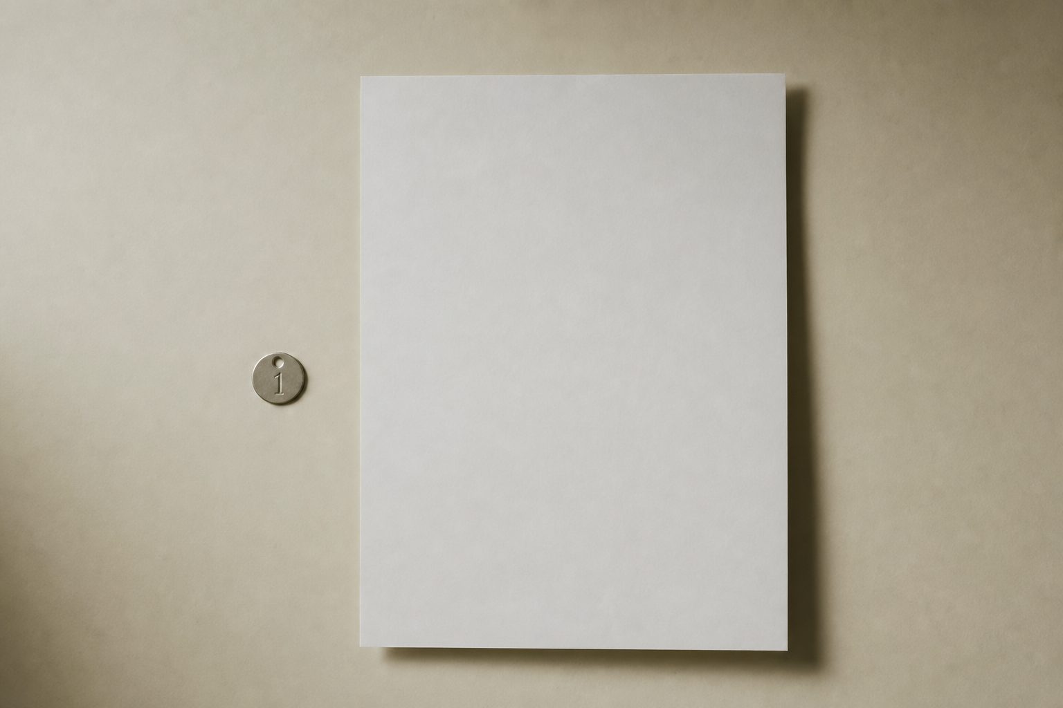 A blank form sheet beside a small stainless identification disc on an ivory surface in grey light
